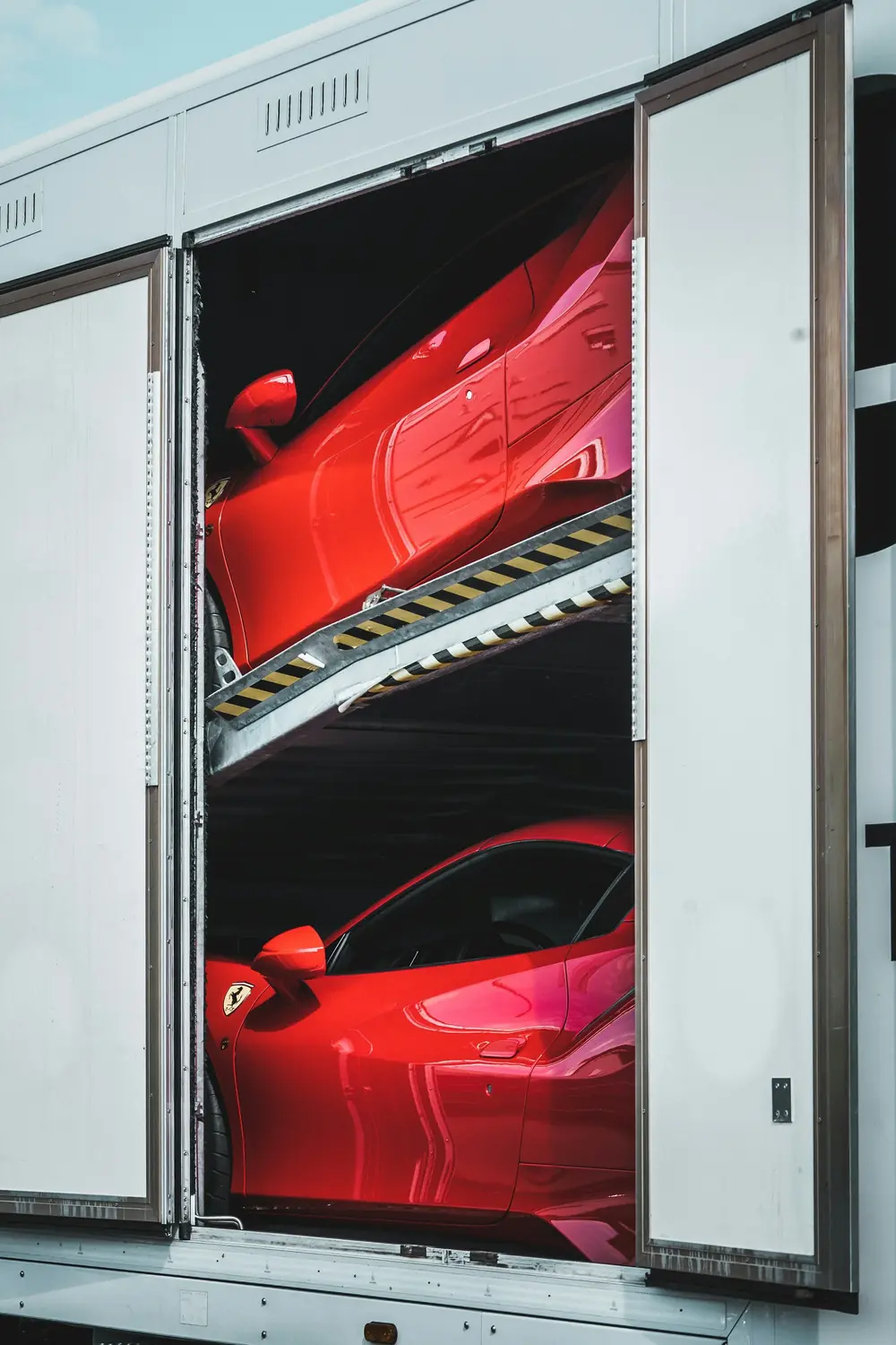 Two red sports cars on the upper and lower decks of an enclosed trailer